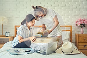 Two Asian female friends using map for route planning of summer vacation trip in hotel room