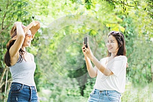 Two Asian female taking photo by smart phone happy traveling in a beautiful park