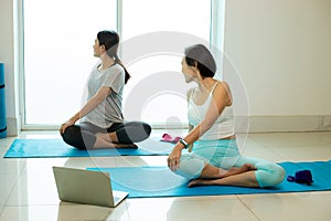 Two Asian female trainer trainee practise yoga pose Seated Twist on blue mat