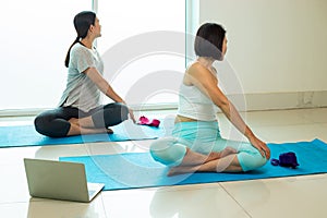 Two Asian female trainer trainee practise yoga pose Seated Twist on blue mat following vdo