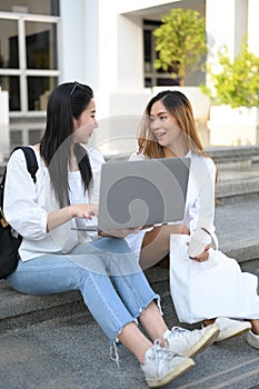 Two Asian female university students sitting at the outdoor building stairs