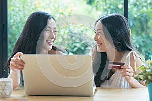 Two Asian friends buying online with credit card and a laptop.