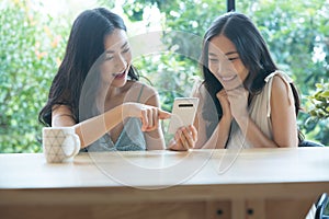 Two Asian friends using mobile phones together while sitting at the cafe.