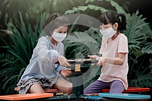 Two Asian girl kids wearing a mask playing with a carousel and having fun in the garden