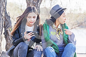 Two asian girlfriends teen girls sit in the park and watch the phone, the generation of digital