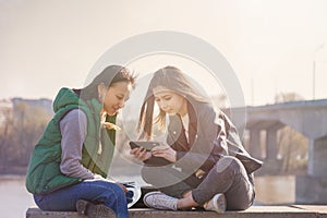 Two asian girlfriends teen girls sit in the park and watch the phone, the generation of digital