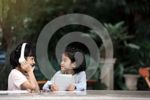 Two Asian girls kids are happily listening to music from the smartphone in the garden