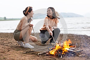 Two Asian girls making bonfire enjoy camping near lake relax vacation. Female enjoy fun in holiday