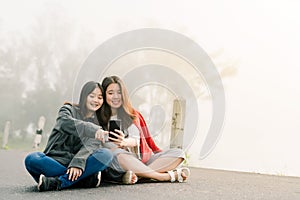Two asian girls Very close friends Wearing a sweater, take a selfie phone, take pictures in a tourist attraction Along the road