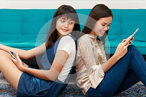 Two Asian grils looking at smatphone and tablet