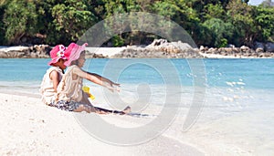 Two asian little child girls sitting and playing with sand together on the beach near the beautiful sea in summer vacation