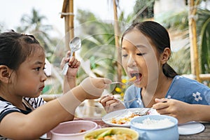 Two asian little girl eating food from pinto