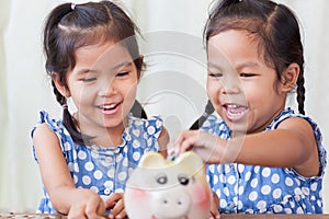 Two asian little girls having fun to put coin into Piggy Bank