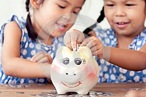 Two asian little girls having fun to put coin into Piggy Bank