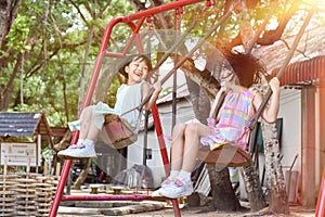 Two asian little sisters having fun on swing together in park on sunny day outdoor. Selective focus