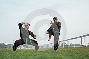 Two Asian men in pencak silat uniforms pose with a stance