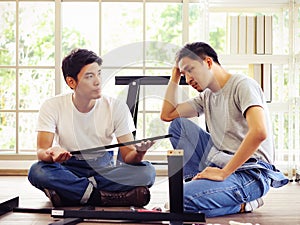 Two  Asian men trying to assemble knockdown furniture and getting confused