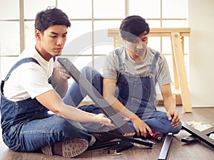 Two  Asian men trying to assemble knockdown furniture and getting confused