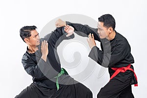 Two Asian men wearing pencak silat uniforms fight with punching and tangkisan atas movements