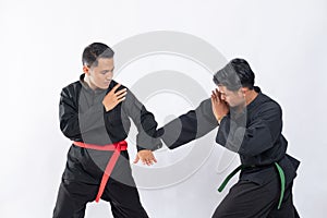 Two Asian men wearing pencak silat uniforms fight with punching and tangkisan bawah movements