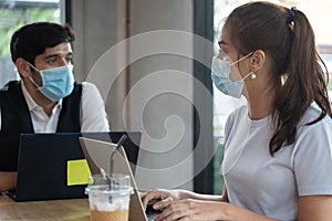 Two Asian people wearing mask meeting working with laptop at coffee shop.