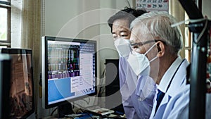 Two Asian senior doctor health care technician looking at patient information and discussing computer screens