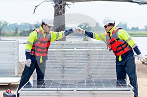 Two Asian technician worker stand beside solar cell panel and show hands bump to each other in concept of green energy system and