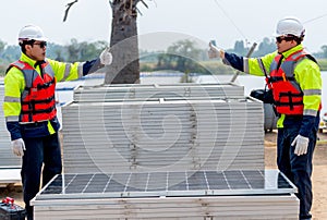 Two Asian technician worker stand beside solar cell panel and show thumbs up to each other in concept of green energy system and