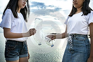 Two asian teenager holding old waste plastic bottle standing on sea beach for ocean environmental issue