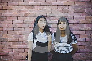 two asian teenager standing in front of red brick wall with surprising face