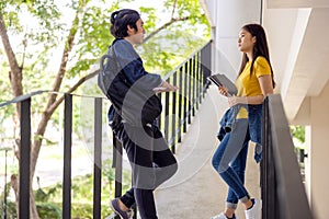 Two Asian university students walking and conversing to class in a magnificent campus building`s walkway