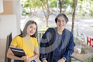 Two Asian university students walking and conversing to class in a magnificent campus building`s walkway