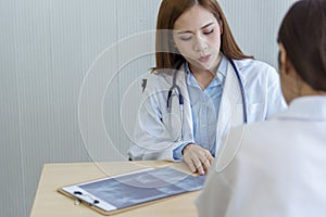 Two asian women doctors discuss meeting doctor`s office medical clinic looking x-ray film consulting patient disease. Asian
