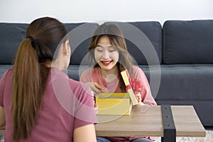 Two Asian women enjoy opening a gift box received for a special occasion. Party, people and new year holidays concept