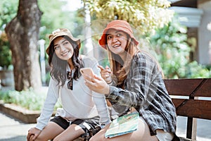 two Asian women in hats chatting about tourist destinations using mobile phones