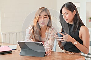 Two asian women holding a coffee cup and using a laptop are discussing plans for her next project