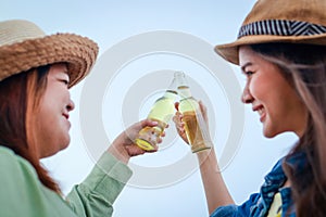 Two Asian women partying at evening beach holding beer bottles smiling happy having fun together.