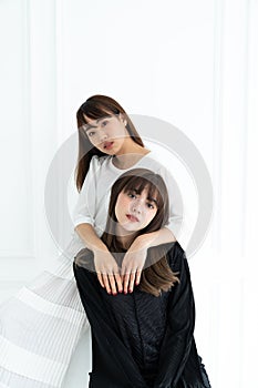 Two asian women sit and laying on each other in pure black and white costume in white backgroud / contrast concept / fashion