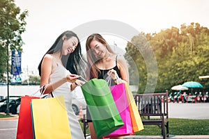 Two asian women standing at outlet mall and looking inside shopping bags paper.