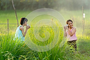 Two Asian young girls enjoy to play with can phone as toy in rice field with warm light and they look happy together