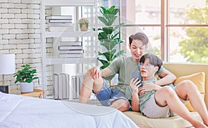 Two Asian young handsome pride male gay men lover couple partner sitting smiling laying down together on cozy sofa in bedroom