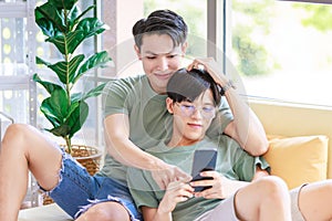 Two Asian young handsome pride male gay men lover couple partner sitting smiling laying down together on cozy sofa in bedroom