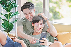 Two Asian young handsome pride male gay men lover couple partner sitting smiling laying down together on cozy sofa in bedroom