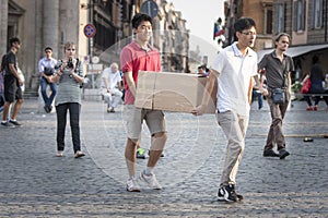 Two Asians carrying large cardboard box in the city downtown