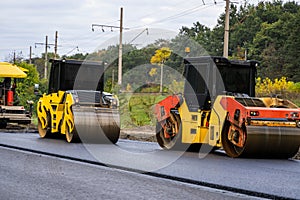 Two asphalt rollers compacting fresh pavement during road construction project