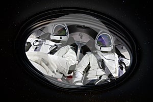 Two astronauts in porthole in space.