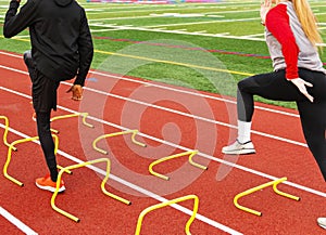 Two athletes running over yellow mini hurdles on a track