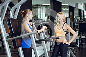 Two athletic blond women talking in the gym. Girl communicates with trainer