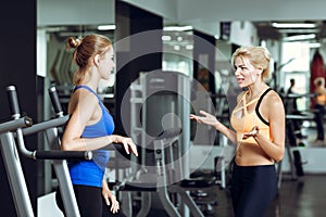 Two athletic blond women talking in gym. Girl communicates with trainer