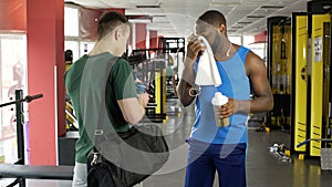 Two athletic men talking at fitness club, sportsmen drinking protein cocktails